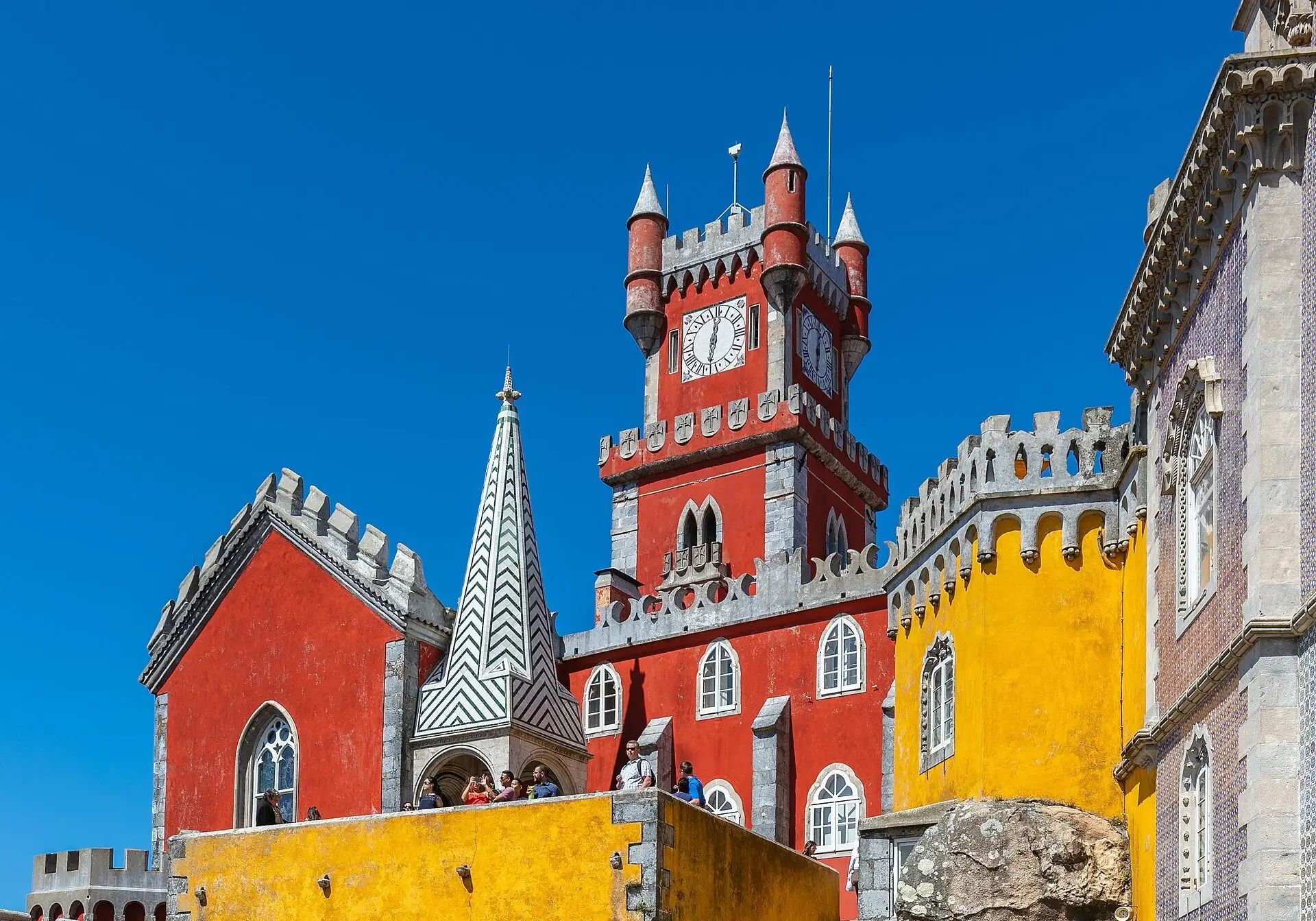 The red clock tower and yellow walls of the Pena Palace in Sintra under a deep blue sky