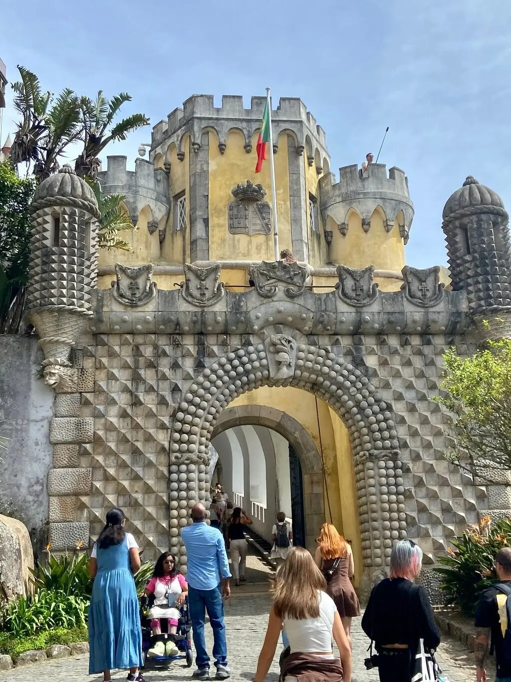 Visitors, one in a wheelchair, walking through the carved gateway into the Pena Palace
