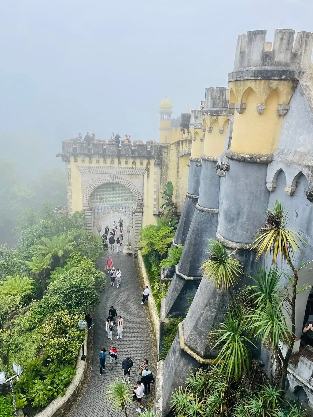 Visitors on the paved path below the Pena walls on a foggy day