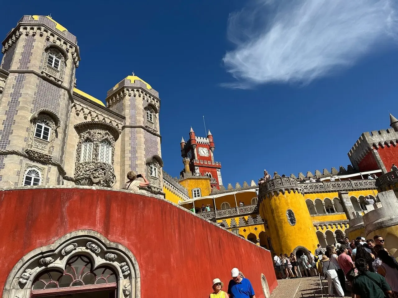 Visitors climbing a busy staircase between the red and yellow walls of the Pena Palace